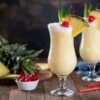 Piña Colada servida en vaso alto con rodaja de piña, cereza y coco, un cóctel tropical refrescante ideal para el verano madrileño.