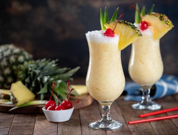 Piña Colada servida en vaso alto con rodaja de piña, cereza y coco, un cóctel tropical refrescante ideal para el verano madrileño.